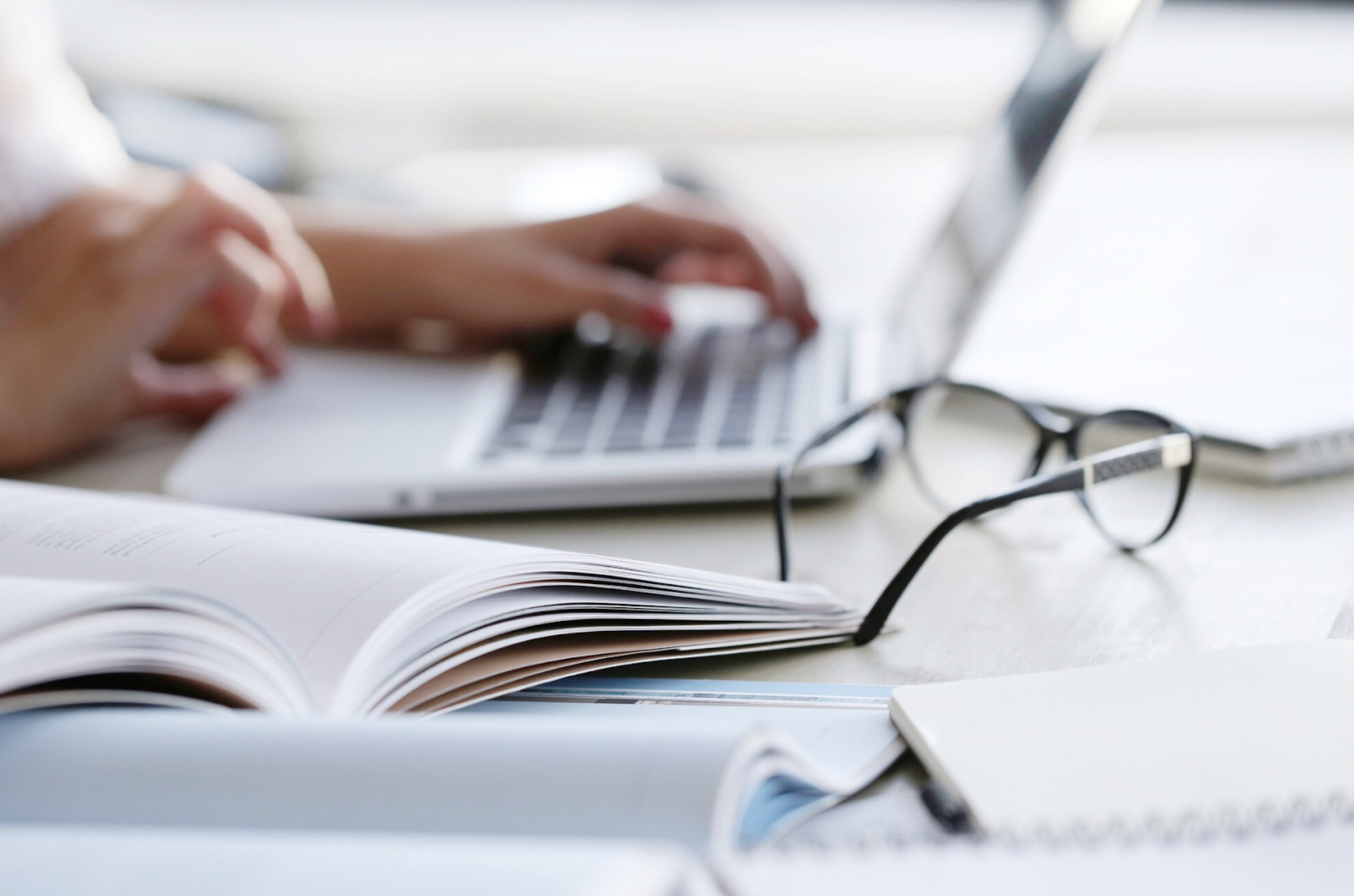 Photo of woman working on computer with papers and glasses on table