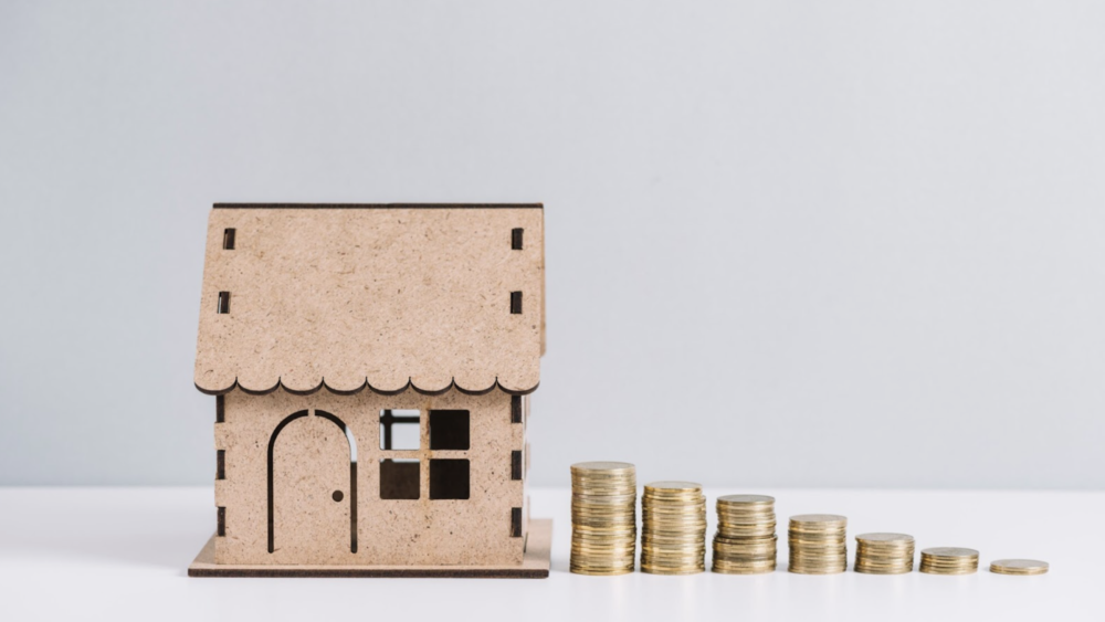 Stacked coins near house model against white background